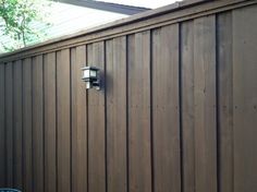 a brown wooden fence with a light on it's side and trees in the background