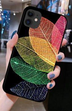 a woman holding up her phone case with colorful leaves on it