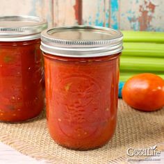 two jars filled with tomato sauce sitting on top of a table next to some vegetables