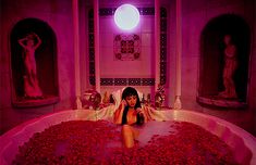 a woman sitting in a bathtub filled with rose petals next to statues and lights