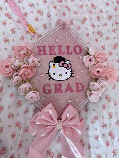 a pink graduation cap with hello kitty on it and flowers around the edges that says hilo grad