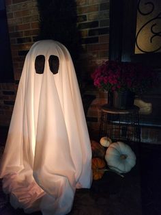 a lighted ghost sitting in front of a brick wall with pumpkins on the ground