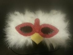 a red and white mask with feathers on it's head, sitting on a black surface