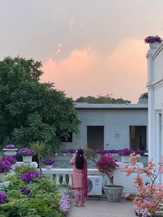 a woman standing in the middle of a garden with lots of purple flowers and potted plants