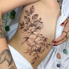 a woman's stomach with flowers and leaves tattooed on the side by her arm