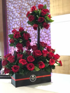 a bouquet of red roses in a black box on a table with a purple wall behind it