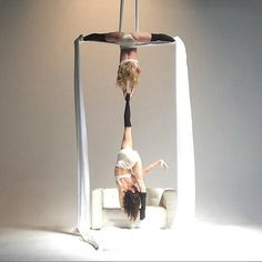 two women doing aerial acrobatic tricks on a white couch in an empty room