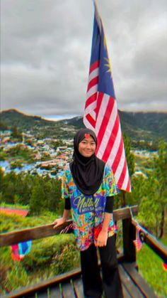 a woman in hijab holding an american flag on a wooden deck overlooking a city