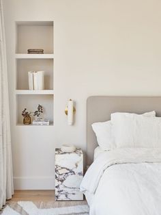 a bed with white sheets and pillows next to a book shelf on the wall above it