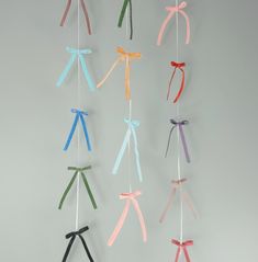 several different colored ribbons hanging from a string on a white wall in the shape of bowes