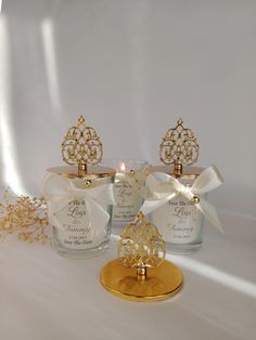 three small glass bottles with gold accents and bows on the top one has a candle in it