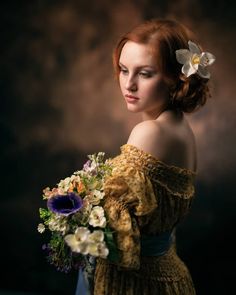 a woman with red hair holding a bouquet of flowers in her left hand and looking off to the side