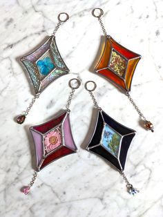 four different colored glass pendants on a white marble counter top with silver chains hanging from them