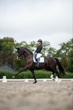 a woman riding on the back of a brown horse across a field with trees in the background