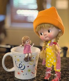 there is a small doll next to a coffee cup