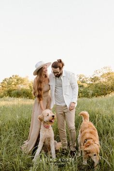 a man and woman standing in tall grass with two dogs