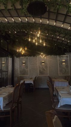 an empty restaurant with tables and chairs covered in white tablecloths, hanging from the ceiling