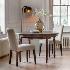 a dining room table with two chairs and a vase on it, in front of a window