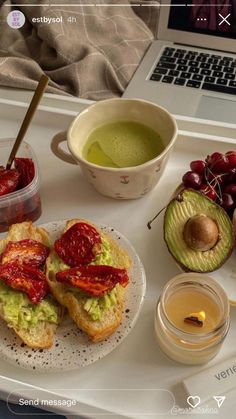 an open laptop computer sitting on top of a white tray filled with sandwiches and fruit