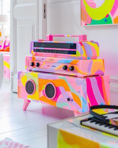 an old fashioned radio sitting on top of a table in front of a wall with colorful paintings