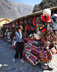 a woman is standing in front of a store selling hats and other items for sale