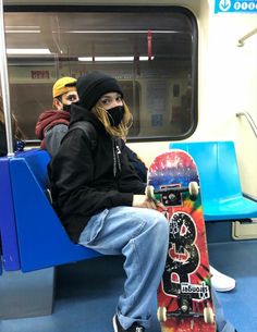 two people sitting on a subway car with their skateboards in hand and one person wearing a face mask