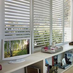 a tv sitting on top of a white shelf next to a window covered in blinds