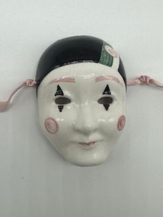 a white mask hanging on the wall with black eyes and pink nose tape around it