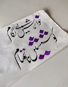 an arabic calligraphy is displayed on a piece of white paper with purple and black writing