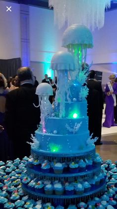 a large blue cake with jellyfish on top and cupcakes around it in the middle