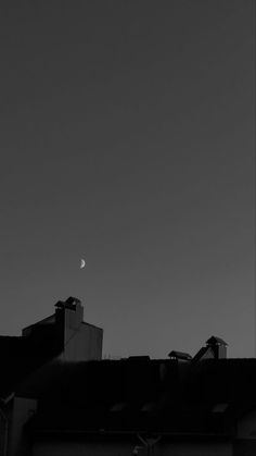 a black and white photo of the moon in the sky over rooftops with buildings