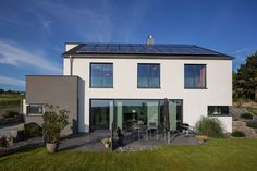 a modern house with solar panels on the roof and glass doors, surrounded by green grass