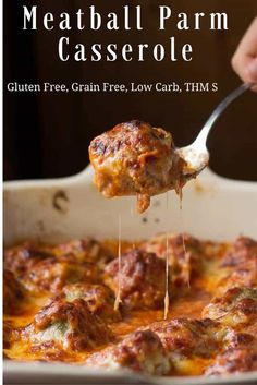 a spoon full of cheese covered meatballs being lifted from a casserole dish