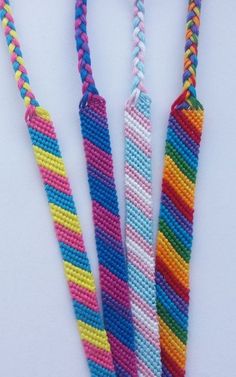 three multicolored necklaces are shown on a white surface and one has a blue, pink, yellow, green, purple, and red striped cord