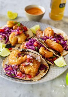 three fish tacos with cole slaw and lime wedges on a white plate