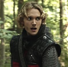 a young man dressed in medieval armor standing in the woods