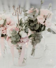 wedding centerpieces with pink flowers and greenery in mason jars on a table