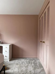 a bedroom with pink walls and carpeted flooring, white furniture and drawers in the corner