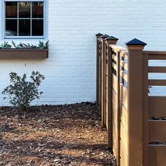 a wooden fence next to a white brick building with a small tree in the yard