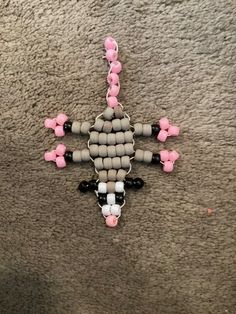 a cross made out of beads is laying on the floor with pink and black beads