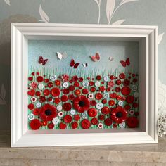 a white frame with red flowers and butterflies in it on a shelf next to a wall