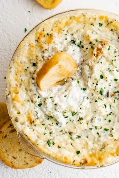 a bowl filled with dip and crackers on top of a white table next to bread