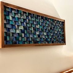 a wooden frame hanging on the side of a wall with blue and green tiles in it