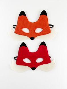 two red and white masks with black ears on top of each other, one in the shape of a fox