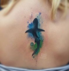 the back of a woman's shoulder with a bird painted on it and watercolor splashes