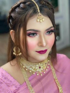 a woman wearing a pink outfit with gold jewelry on her head and necklaces around her neck