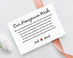 a card that reads our honeymoon wish next to a white carnation and pink ribbon