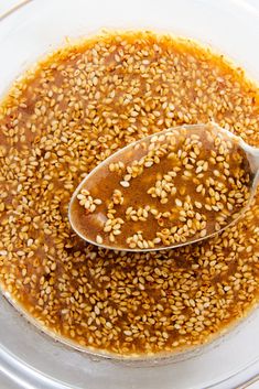 sesame seeds in a glass bowl with a spoon full of brown sauce on the side