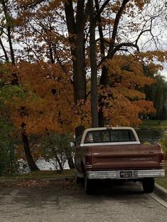 an old truck is parked in front of some trees with orange leaves on the ground