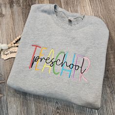 Welcome to my shop! This listing is for an embroidered crewneck sweatshirt!  *Sweatshirt is a Bella Canvas drop shoulder pullover in heather gray. Sizing runs unisex, these are a high quality sweatshirt with long sleeves and torso (see size chart in photos). Other sweatshirt colors may be done upon request for an additional fee. *Front design is TEACHER in rainbow colors! Personalized in script black font is your choice of grade! Feel free to message me for any custom requests! Can change any wording or colors! PaigesStitches Shop Notes: Thank you for visiting my shop! Here are a few things to read before checking out. -All sales are final, I do not offer exchanges or returns. If there is an issue with your order, please contact me! -Packages 1 pound or less ship USPS First Class Mail, all Customizable Crew Neck Sweatshirt For School, Casual Customizable Sweatshirt For School, School Sweatshirt With Embroidered Text And Crew Neck, Cotton Sweatshirt With Embroidered Text For School, School Crew Neck Sweatshirt With Embroidered Text, School Sweatshirt With Embroidered Logo, Teacher Embroidered Shirt, Teacher Embroidery Sweatshirt, Rainbow Prek Shirt